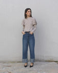 Une femme portant un pull à volants beige clair accompagné d'un jean tendance. Ce modèle de pull maille fine femme apporte élégance et confort pour toutes les occasions.