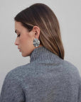 Femme de profil mettant en avant le pull col roulé femme gris et des boucles d'oreilles modernes.