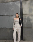 Model avec un pull épaule dénudée beige en tricot, porté avec un pantalon beige, illustrant une mode contemporaine et élégante.