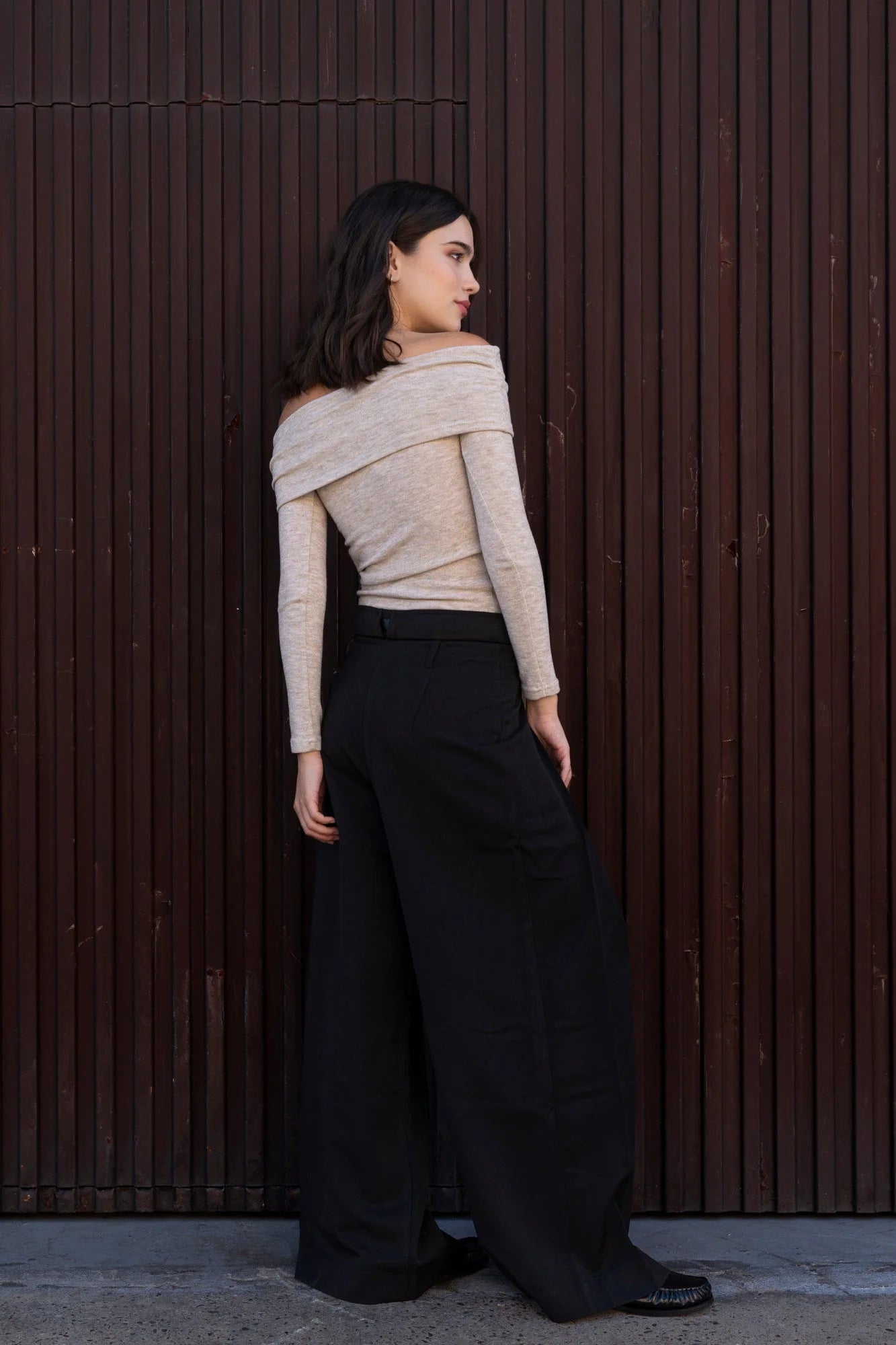 Femme portant un pull épaules dénudées beige et pantalon noir large-leg