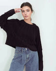 Femme posant avec le pull laine femme noir à torsades, mettant en avant son originalité avec des motifs, confort élevé pour l'hiver.