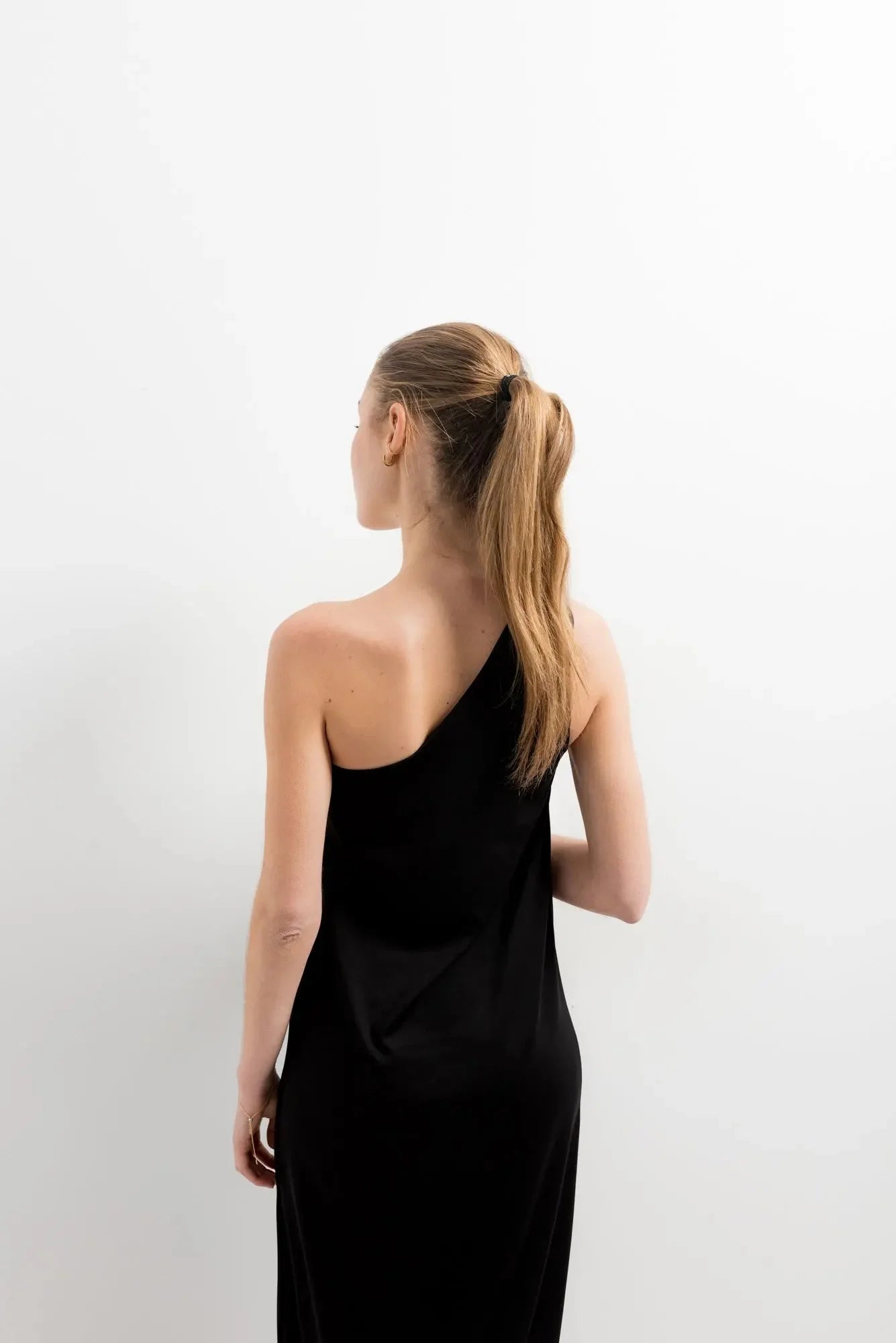 Femme en robe asymétrique bijou noire avec queue de cheval, idéale pour occasions spéciales