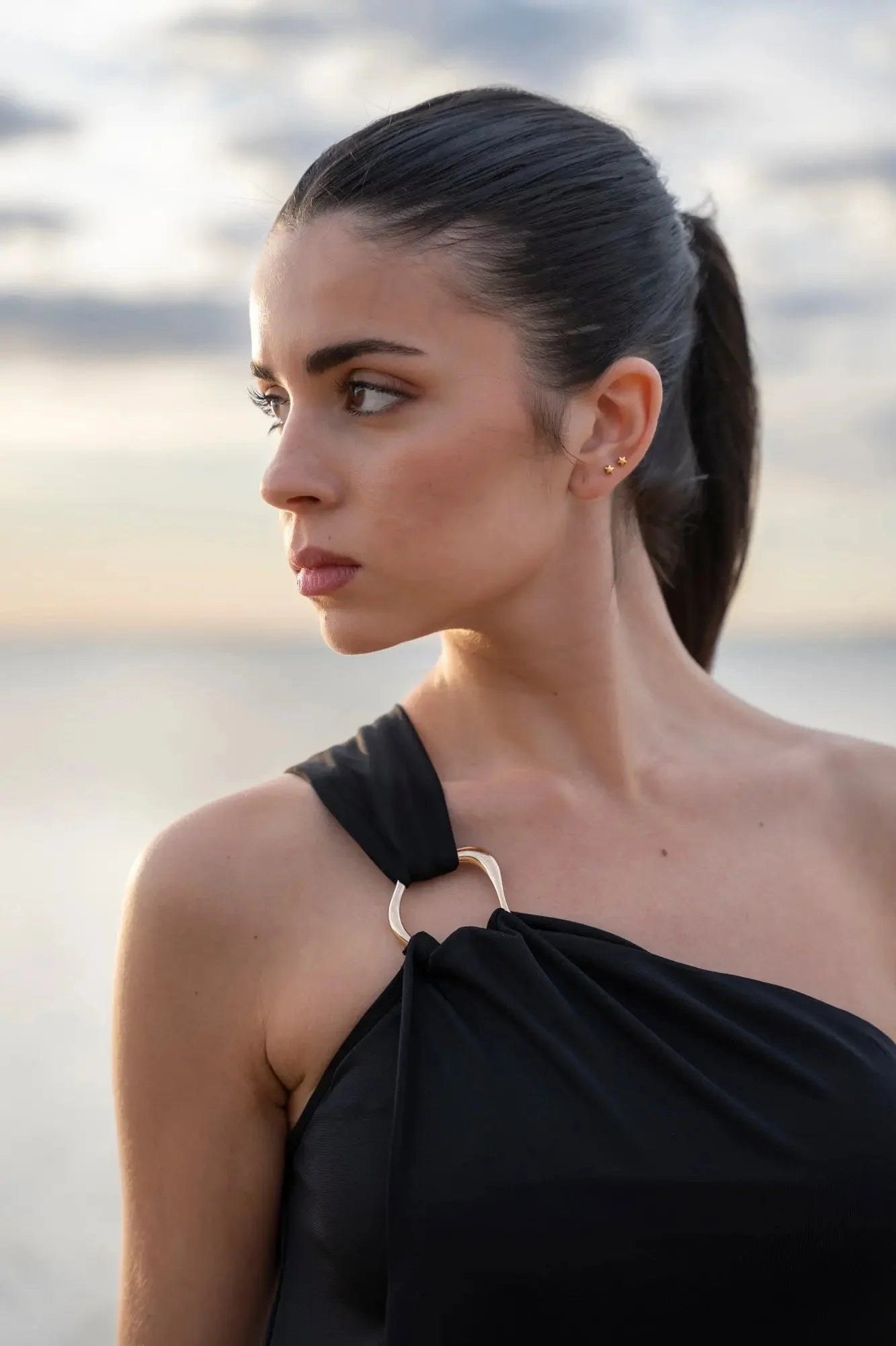 Femme portant une robe asymétrique bijou noire avec détail en anneau or pour occasions spéciales
