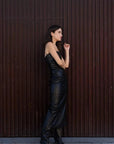 Femme en robe longue simili cuir noir bustier midi avec fente latérale - Élégance Audacieuse, dans une pose contemporaine.