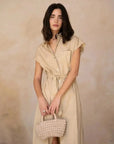 Modèle portant une robe chemise femme beige midi ceinturée, mettant en valeur son élégance fluide en popeline, avec un sac en paille.