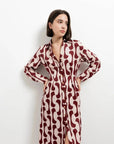 Portrait d'une femme en robe chemise longue imprimée bordeaux, stylée avec des boutons dorés et un col chemise, avec une expression calme.