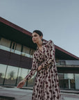 Femme en robe chemise longue imprimée bordeaux, prenant une pose dynamique à l'extérieur, mettant en valeur le design moderne et élégant.