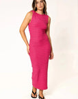 Femme en robe fuchsia moulante midi à rayures texturées, posant avec confiance, montrant son style moderne avec une approche chic.