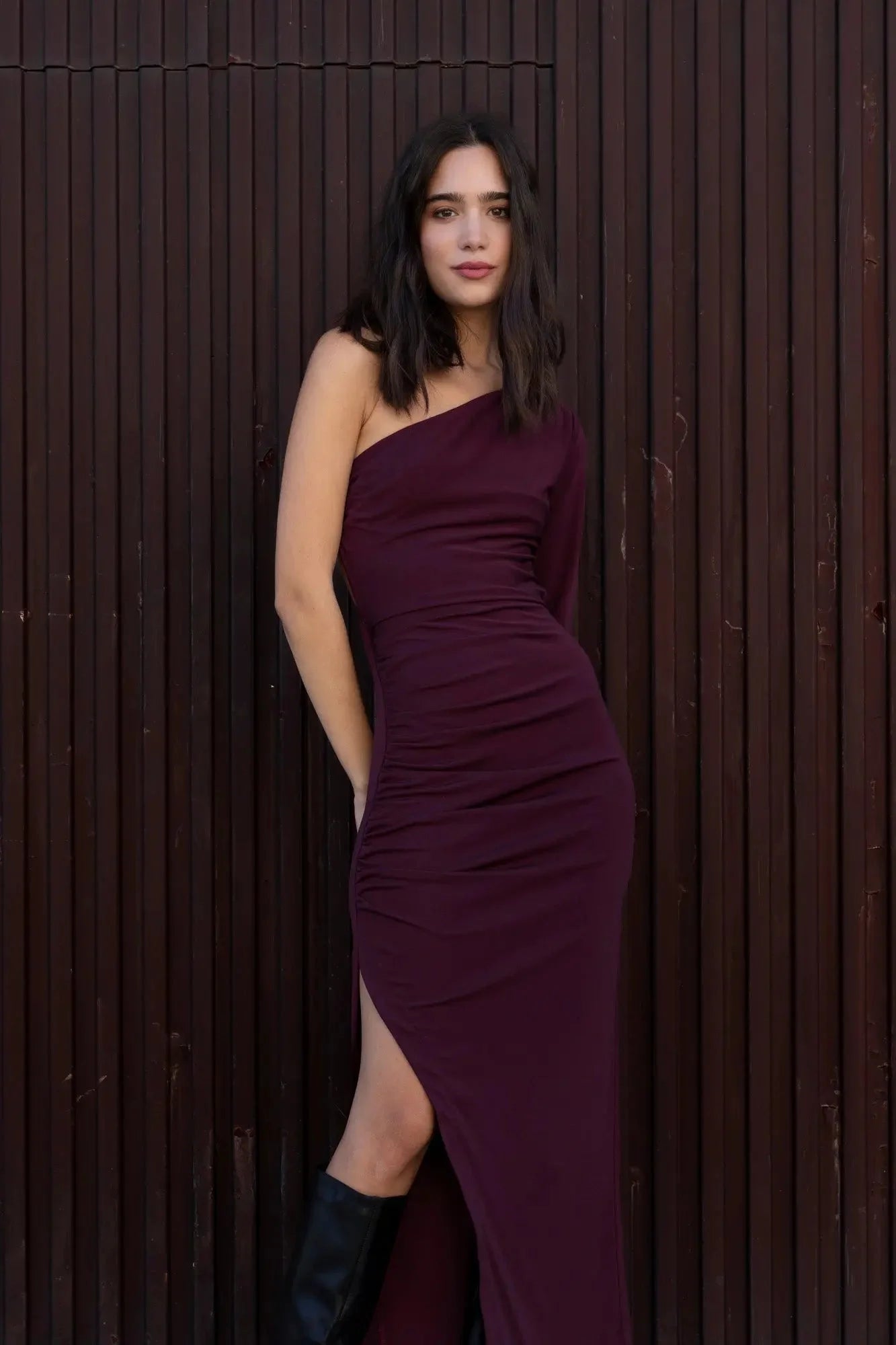 Femme en robe longue asymétrique à manche unique et slit, avec bottes noires