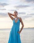 Femme posant élégamment sur la plage dans une robe longue bretelles fines, fluide et légère, idéale pour les soirées d'été.