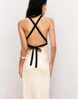 Détails du dos d'un modèle portant une robe longue dos nu en lin écru, montrant les bretelles croisées noires et le nouage, idéale pour un look chic.