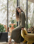 Femme assise dans un espace lumineux, portant une robe longue verte sauge fluide, élégante et chic, idéale pour les sorties décontractées.