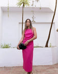 Modèle debout dans une robe fuchsia longue chic en lin, sans manches, encolure froncée, style minimaliste, posé dans un cadre extérieur.