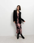Femme stylée avec une robe tie dye longue satinée noir et rose sous un blazer, parfaite pour une soirée.