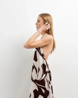 Robe Longue Bohême Imprimée Chocolat & Blanc Dos Nu Fluide avec Col Licou, femme touchant ses cheveux, capturant l'élégance et la fluidité du vêtement.