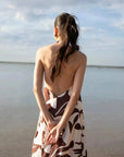 Robe Longue Bohême Imprimée Chocolat & Blanc Dos Nu Fluide avec Col Licou, vue arrière du modèle montrant le dos nu, au bord de la mer.