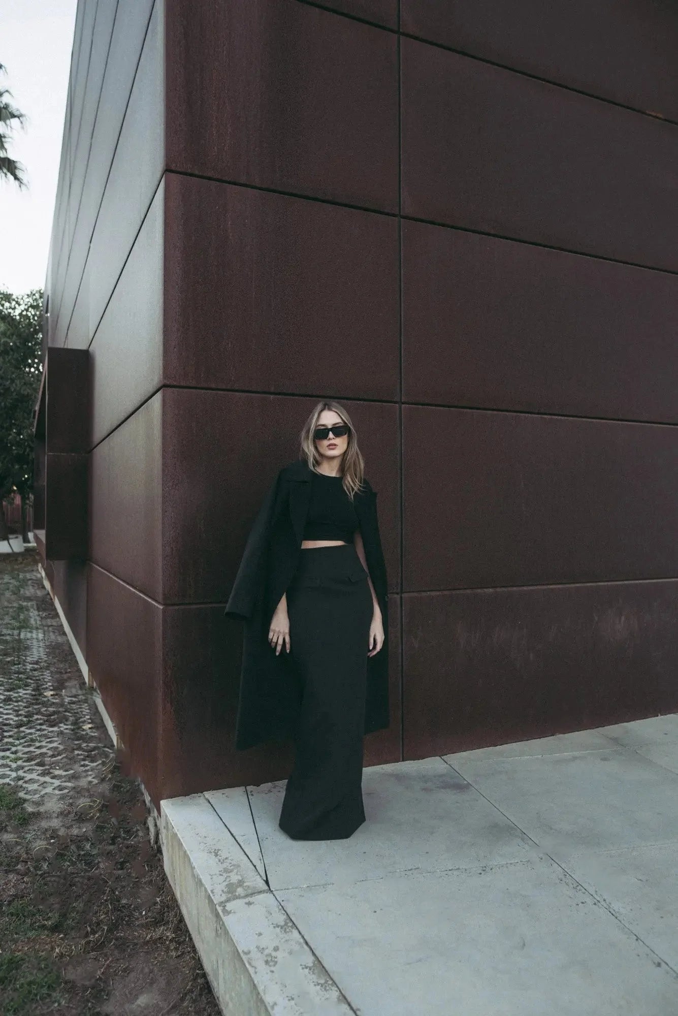 Femme portant une jupe midi avec fente latérale, long manteau et sunglasses élégants
