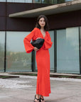 Robe satinée rouge midi croisée avec décolleté plongeant et manches longues évasées, portée à l'extérieur avec une pochette noire.