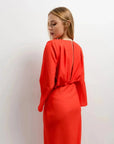 Vue arrière d'une femme dans une robe satinée rouge midi croisée avec décolleté plongeant, mettant en valeur la coupe et le tissu.