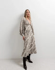 Modèle avec une robe midi imprimé python à col cache-cœur, posant avec style. La coupe fluide et les manches bouffantes soulignent l’élégance de cette robe animal.