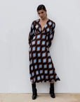 Femme dans une robe motif géométrique midi avec décolleté en V profond, mettant en avant le motif original des couleurs marron, bleu et noir.