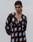 Femme posant dans une robe motif géométrique midi au décolleté V profond et aux manches bouffantes, soulignant son style unique et vibrant.