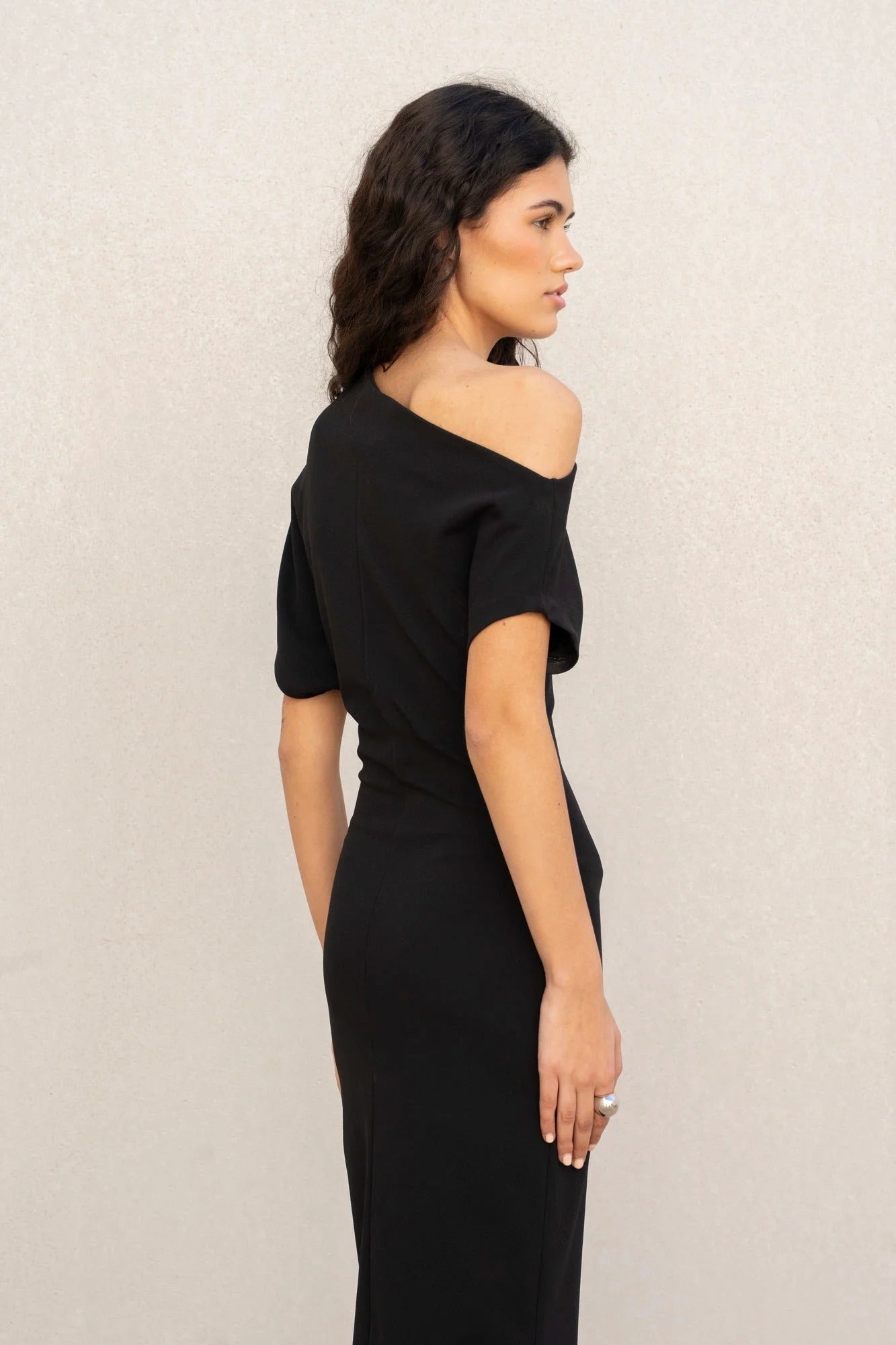 Femme portant une robe noire asymétrique épaule dénudée, coupe midi élégante