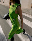 Modèle portant la Robe Verte Chic Midi Sans Manches Avec Pince Dorée, défilant dans une rue, mettant en avant la couleur vive et le style élégant de cette robe verte chic.