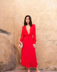 Robe mousseline rouge midi, décolleté plongeant, vue complète d'une femme posant avec une pochette, idéale pour un mariage ou une cérémonie.