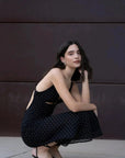 Femme assise dans une pose détendue, vêtue de la robe noire à pois blanc qui souligne la silhouette avec élégance.