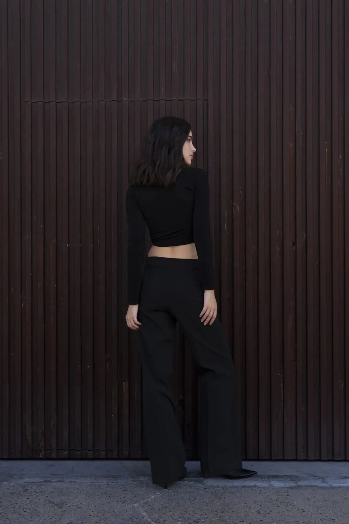 Vue arrière d'une femme en T-Shirt Crop Top Manche Longue Avec Noeud Élégant Pour Femme, combiné avec des pantalons élégants pour un look moderne.