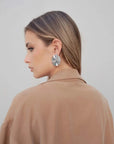 Vue de profil d'une femme en blazer fluide camel avec des boucles d'oreilles modernes.