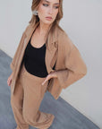 Vue plongeante de la femme en tailleur blazer fluide camel, complété par un haut noir et un pantalon ample.