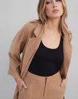 Détail sur un blazer oversize croisé fluide camel porté avec un top noir ajusté.
