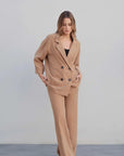 Femme debout en tailleur blazer fluide camel avec un pantalon assorti, posant avec élégance.