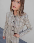 Femme portant un tailleur pantalon à carreaux beige look structuré, style chic avec un col et des boutons sur l'ensemble du haut, parfait pour un look élégant. Pantalon femme carreaux.