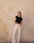 Femme posant contre un mur dans un look décontracté associé à un pantalon ample crème, mettant en lumière le pantalon pince femme.