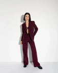 Femme posant avec style dans un blazer femme bordeaux double boutonnage croisé, complété par un pantalon assorti.