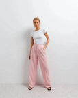 Pantalon rose femme ceinturé pour toutes occasions, femme stylée en tee-shirt blanc et pantalon rose, pose moderne et confiante.