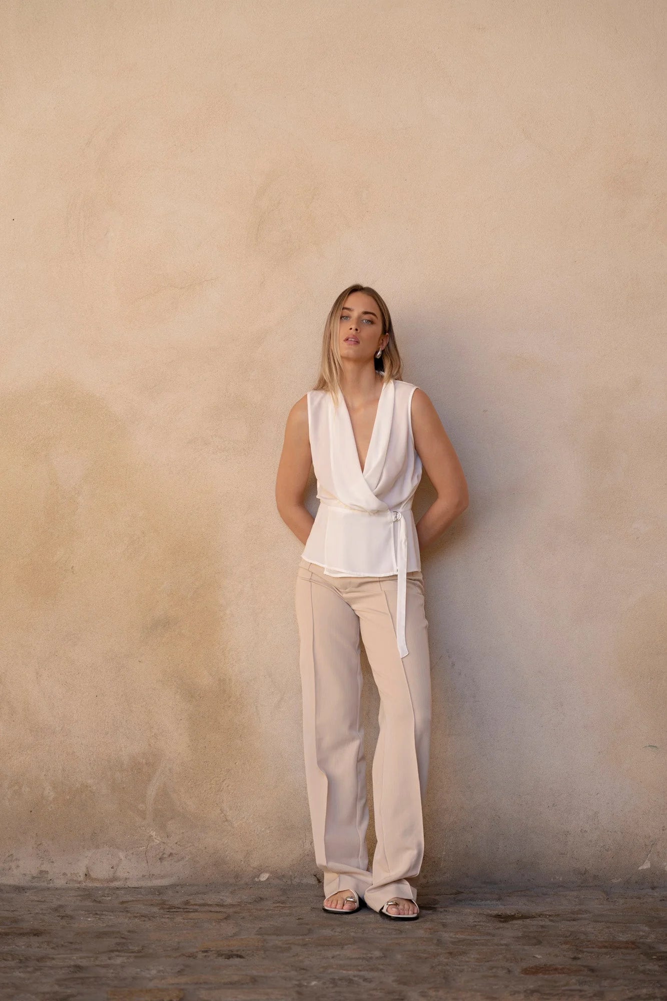 Femme portant un top blanc croisé sans manches, pantalon beige et sandales blanches