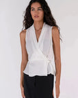 Détail du haut blanc croisé sans manches avec un nœud sur le côté, un ajout chic à la garde-robe des hauts blancs femme.