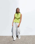 Femme portant un haut col bénitier noué vert lime, stylé avec un pantalon blanc, parfait pour un look décontracté ou chic. Haut col bénitier femme.
