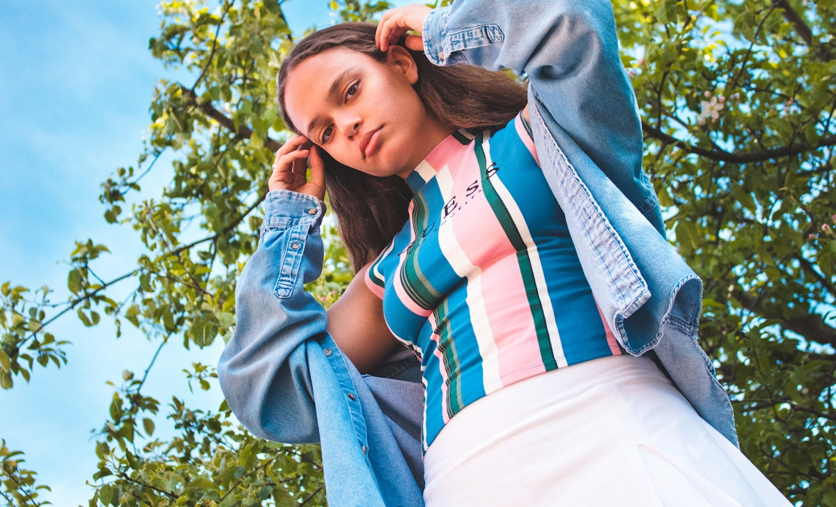 woman in white red and blue striped shirt and blue denim jeans sitting on green grass