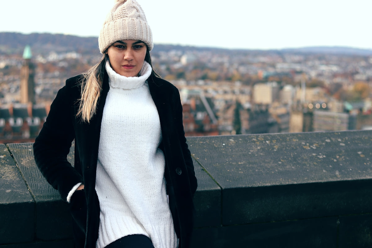 woman in black jacket and gray knit cap sitting on concrete wall during daytime
