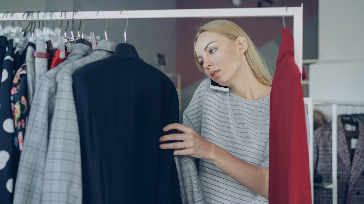 Woman shops for clothes while talking on phone.