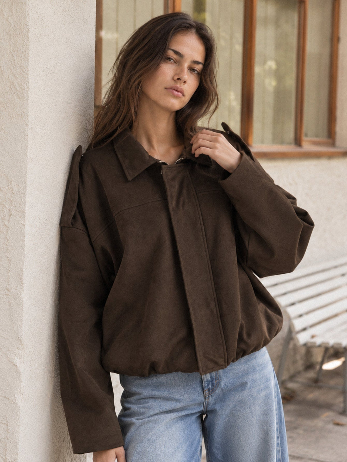 Blouson bomber suédine chocolat posé contre un mur