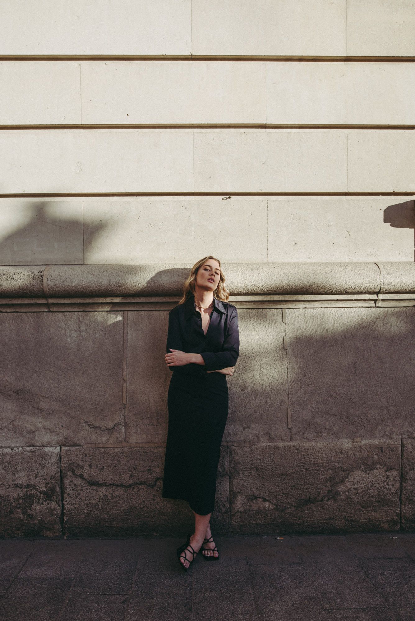 Femme posant en jupe midi marine taille haute devant un mur historique, illustrant le style polyvalent de la jupe midi.