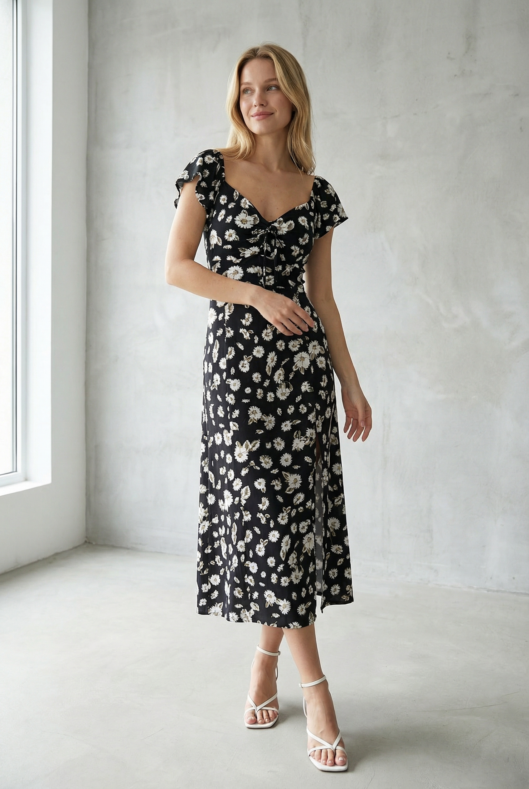 Femme élégante portant une robe longue noire à imprimé floral avec fente latérale, idéale pour des occasions spéciales et un look sophistiqué.