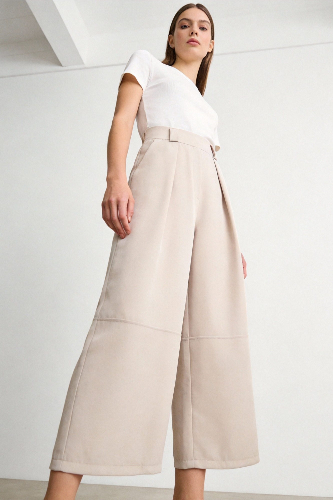 Femme portant un pantalon court plissé taille haute ceinture élastique à poches dans une teinte beige, affichant un style à la fois chic et confortable. Pantalon plissé femme.