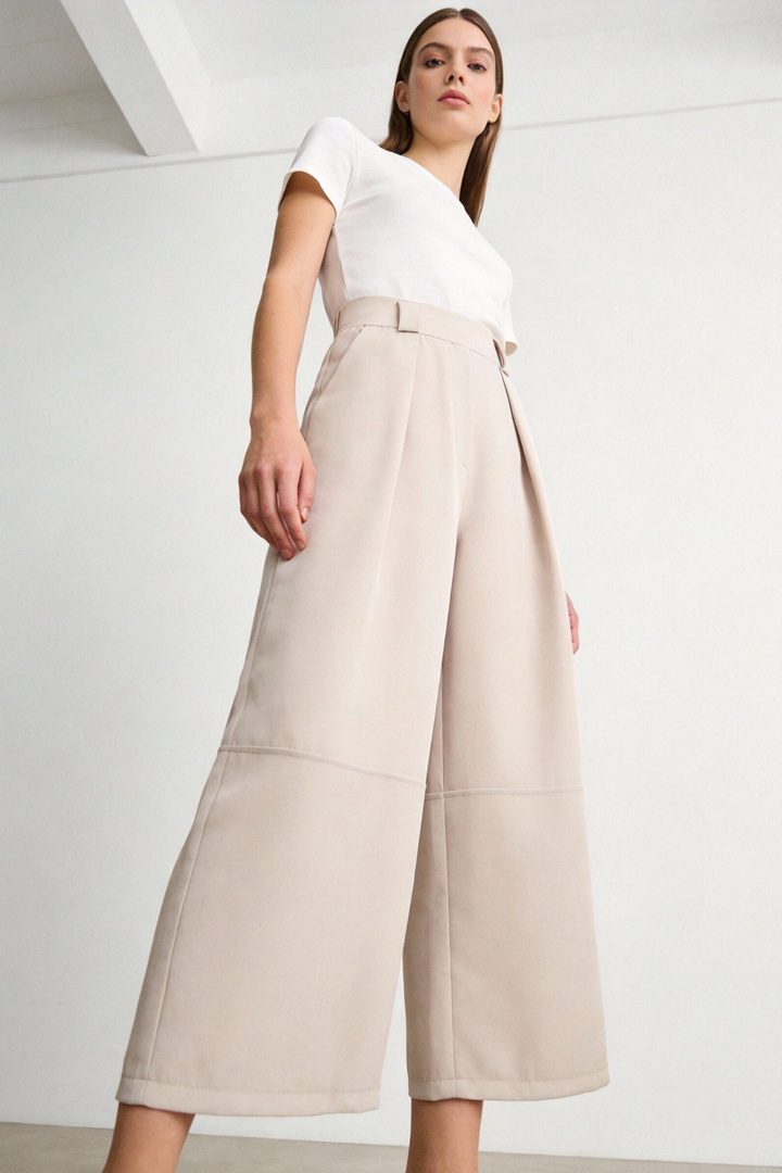 Femme portant un pantalon court plissé taille haute ceinture élastique à poches dans une teinte beige, affichant un style à la fois chic et confortable. Pantalon plissé femme.